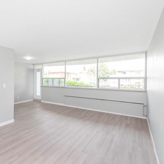 a spacious room with light wood flooring and large windows.