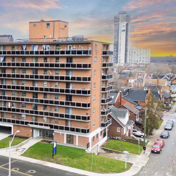 a large apartment building is situated on a street corner with cars parked along the curb.