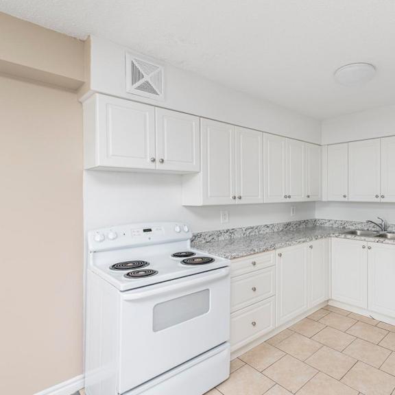 a white kitchen with a stove, sink, and refrigerator.