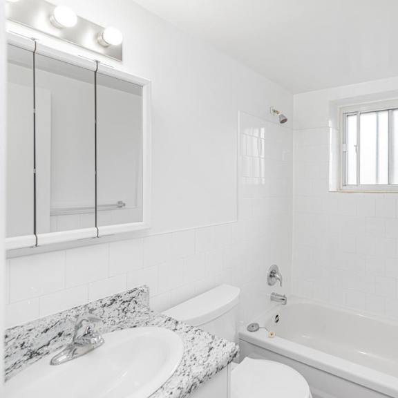 a white bathroom with a marble countertop and a window.
