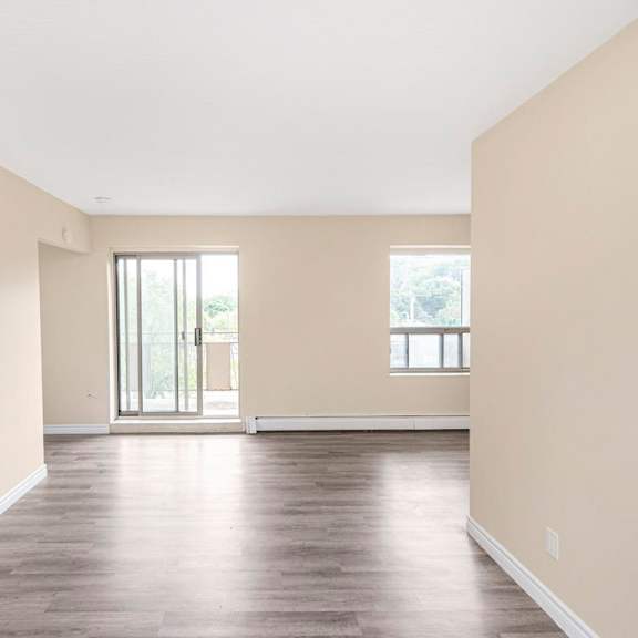 a large empty room with wooden floors and two windows.