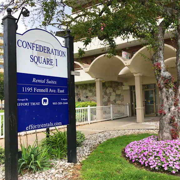a sign for confederation square 1 rental suites stands in front of a building.