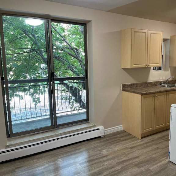 a kitchen with a white fridge, wooden cabinets, and a window with a view of trees.