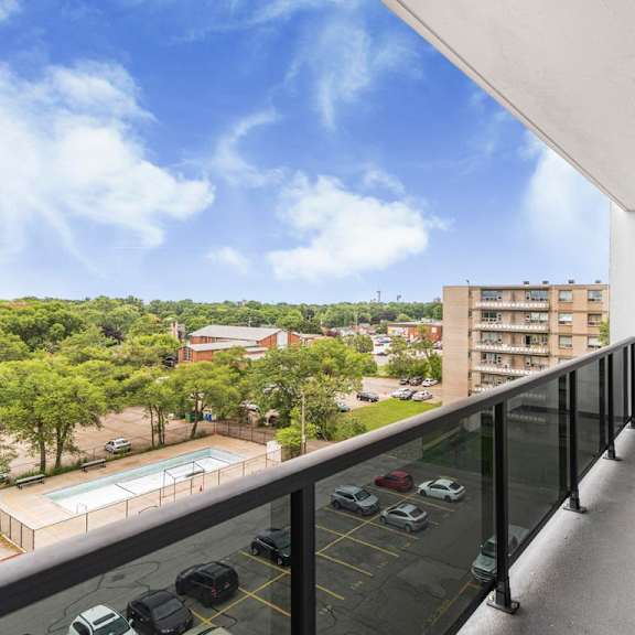 a balcony with a black railing overlooks a parking lot and buildings.