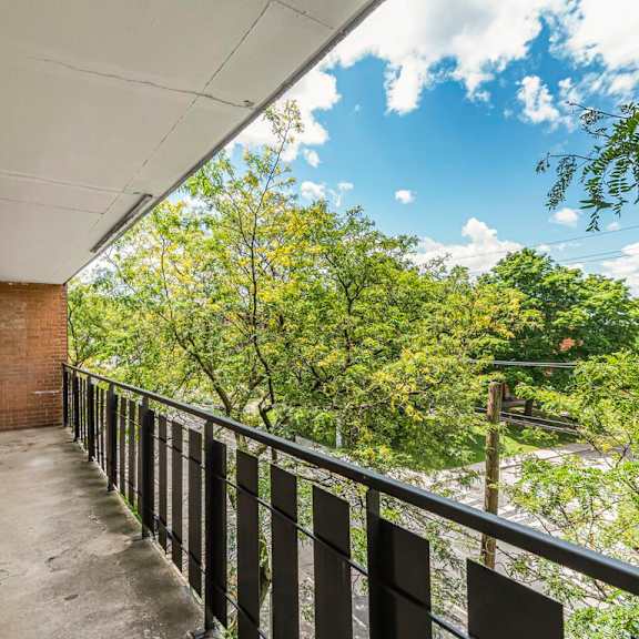 a balcony with a black railing and a view of trees and a blue sky.