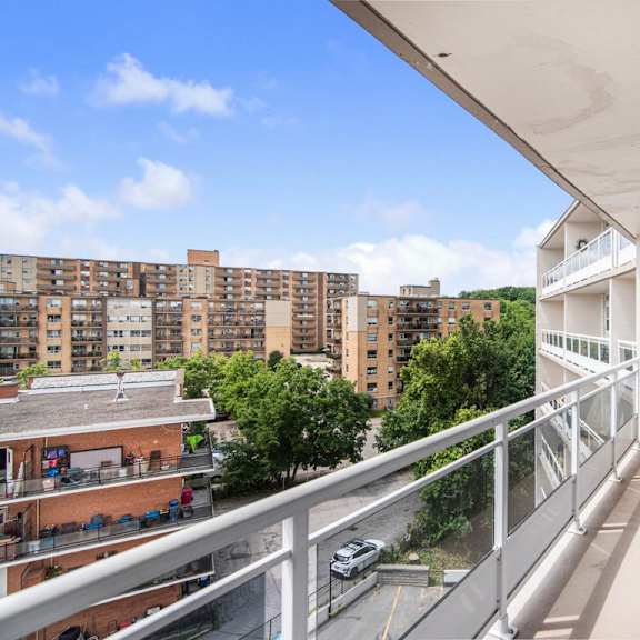 a balcony with a metal railing overlooks a parking lot and apartment buildings.