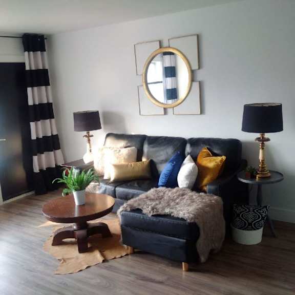 a living room with a black and white striped curtain, a black leather sofa, a wooden coffee table, and a round mirror on the wall.