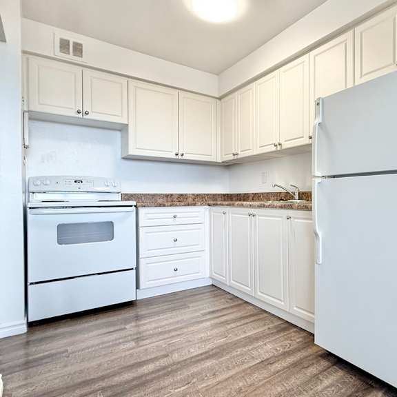 a white refrigerator stands in a kitchen with wooden floors and white cabinets.