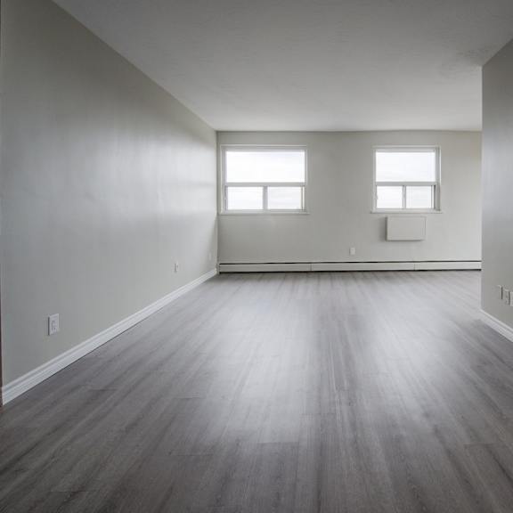 a spacious room with wooden floors and two windows.