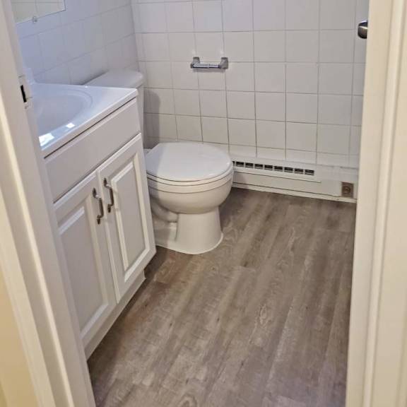 a white toilet in a small bathroom with a wooden floor.