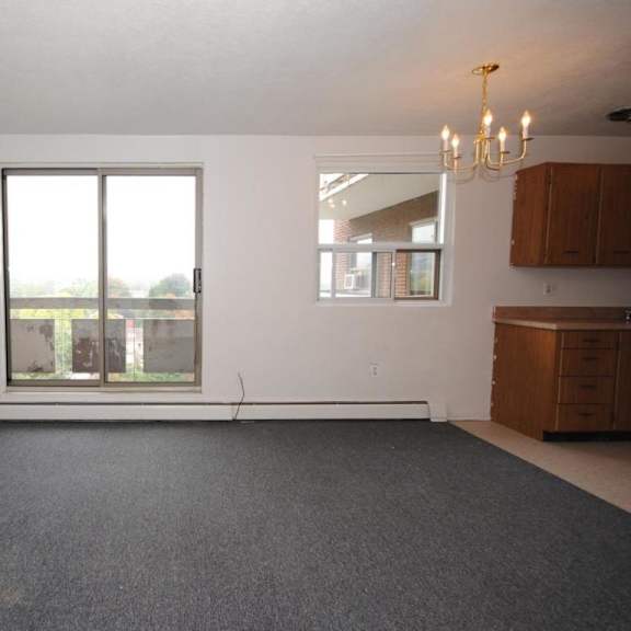 a large empty room with a grey carpet and a chandelier.