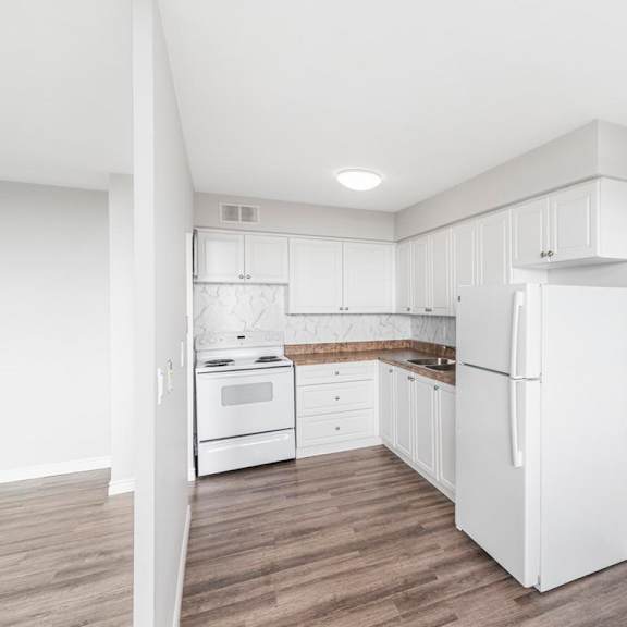 a white kitchen with a refrigerator, sink, and oven.