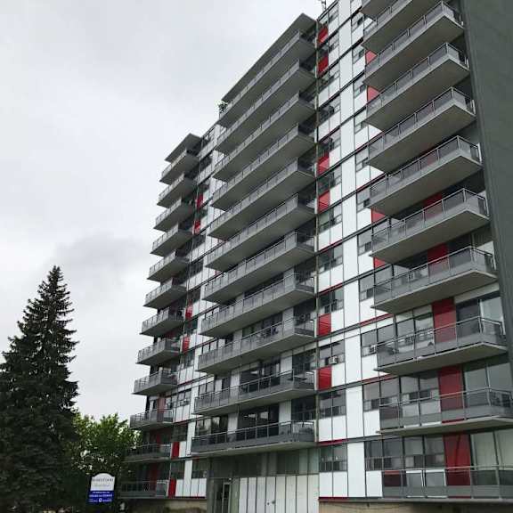 a tall building with balconies and a cloudy sky in the background.