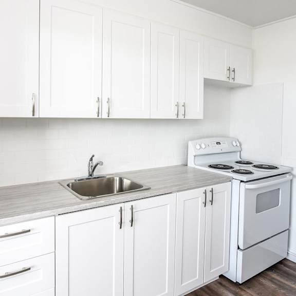 a white kitchen with a stove, sink, and cabinets.