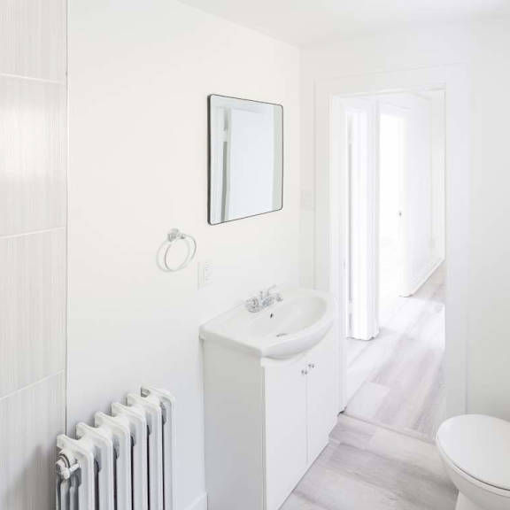 a white bathroom with a toilet, sink, and radiator.