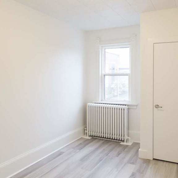 a room with a white door, a window with a white frame, and a white radiator on the floor.