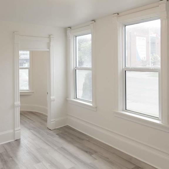 a room with white walls and wood flooring with three windows.