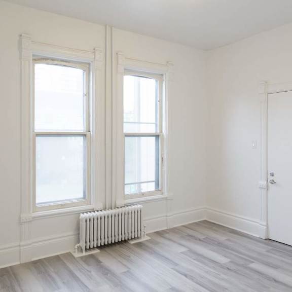 a room with a white door, two windows and a radiator on the floor.