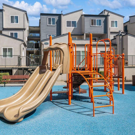 a playground with a slide and swings in front of apartment buildings.