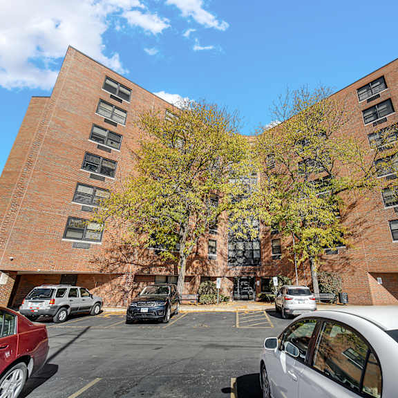 a parking lot with cars and a red car in the foreground at fullerton court apartments, chicago, illinois