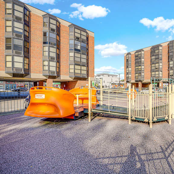 a playground area in front of a building with orange and grey buildings in the background at fullerton court apartments, chicago, 60614