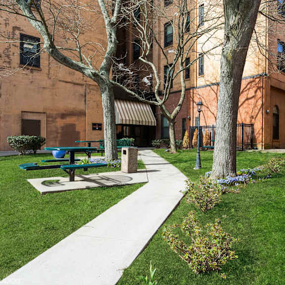 a park with a bench and a tree in front of a brick building at mohican apartments, new london, 06320