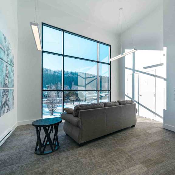 a room with a grey couch, a blue table and a large window.