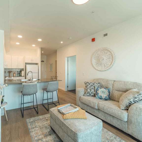 a modern living room with a grey couch and a kitchen area in the background.