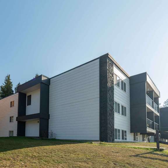 a modern building with a white and black facade is surrounded by a grassy area and trees.