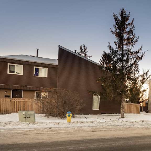 a row of houses with snow on the ground and trees in front.