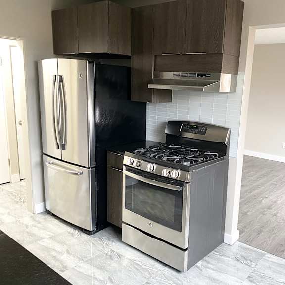 a kitchen with a black fridge, stainless steel oven and a black and white tiled backsplash.
