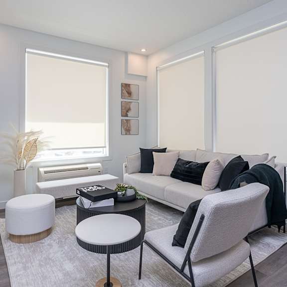 a living room with a white couch, a white ottoman, and a black chair.