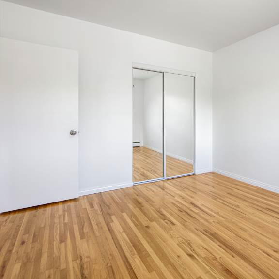 a room with a wooden floor and a white wall with a door and a mirror.