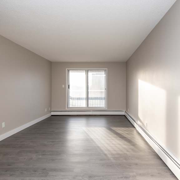 a spacious room with a window and wooden flooring.