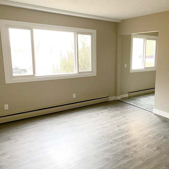 a room with light wood flooring and two windows.
