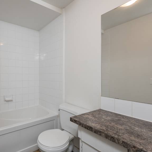 a white bathroom with a toilet, tub, and marble counter.