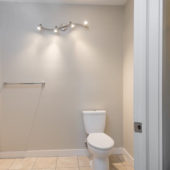 a white toilet in a small bathroom with a shower curtain rod and lights above it.