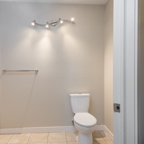 a white toilet in a small bathroom with a shower curtain rod and lights above it.