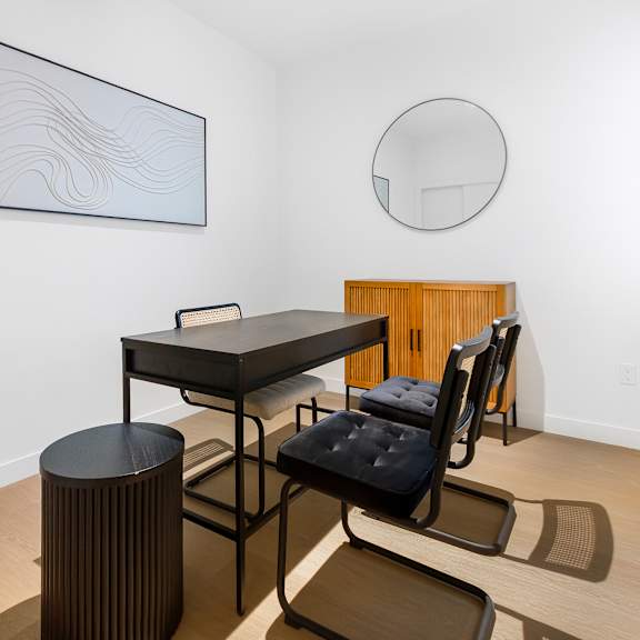 a black chair with a black cushion is in front of a black table with a black chair and a black stool.