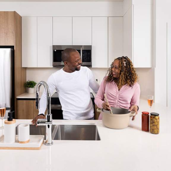 a man and woman are standing in a kitchen with a sink and a refrigerator.