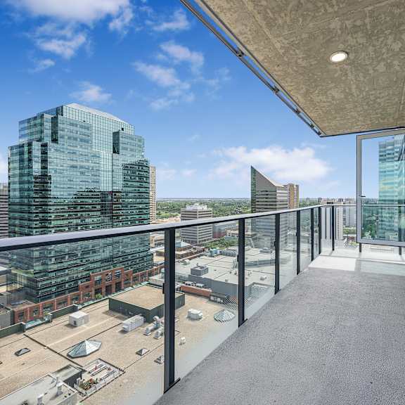 a long balcony with glass railings overlooks a cityscape.