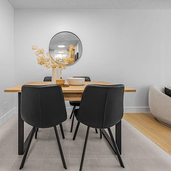 a dining table with two chairs and a round mirror above it.