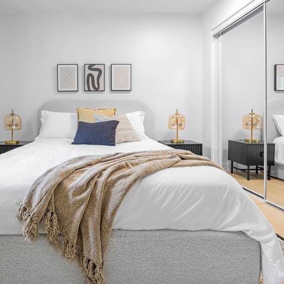 a bedroom with a large bed covered in a white duvet and a beige throw.