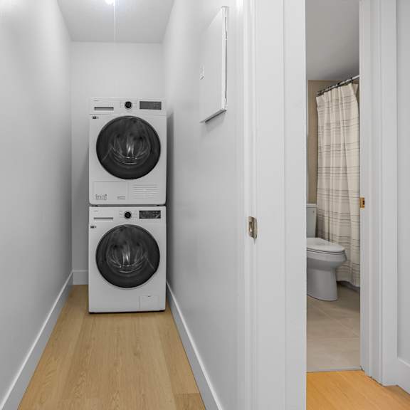 a white dryer and washer are stacked on top of each other in a small, white-walled laundry room.