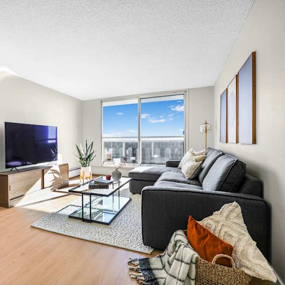 a living room with a grey couch, a red chair, a glass coffee table and a television.