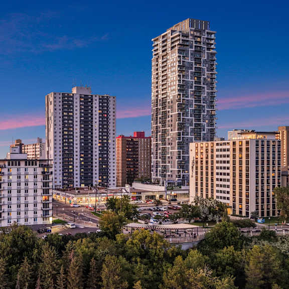 a cityscape with tall buildings and a parking lot in the foreground.