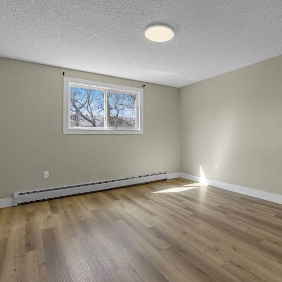 a room with wooden flooring and a window showing a tree outside.
