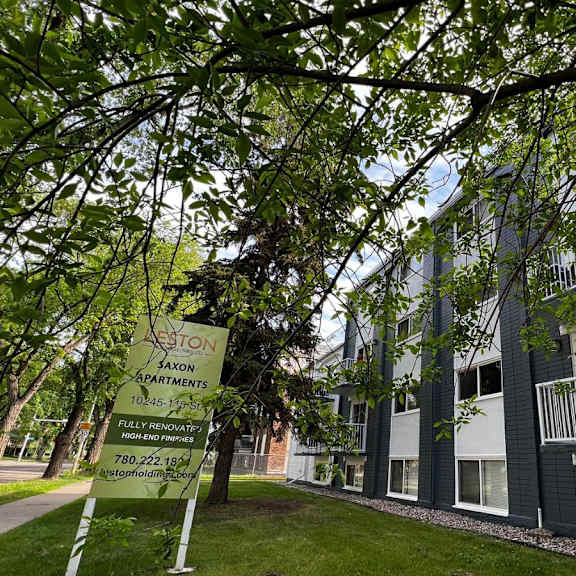 a tree branch is in the foreground of a photo showing a sign for saxon apartments.