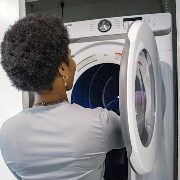 a woman with short hair is putting something into a washing machine.