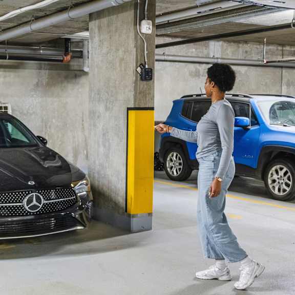 a woman is walking past a black mercedes-benz car in a parking garage.